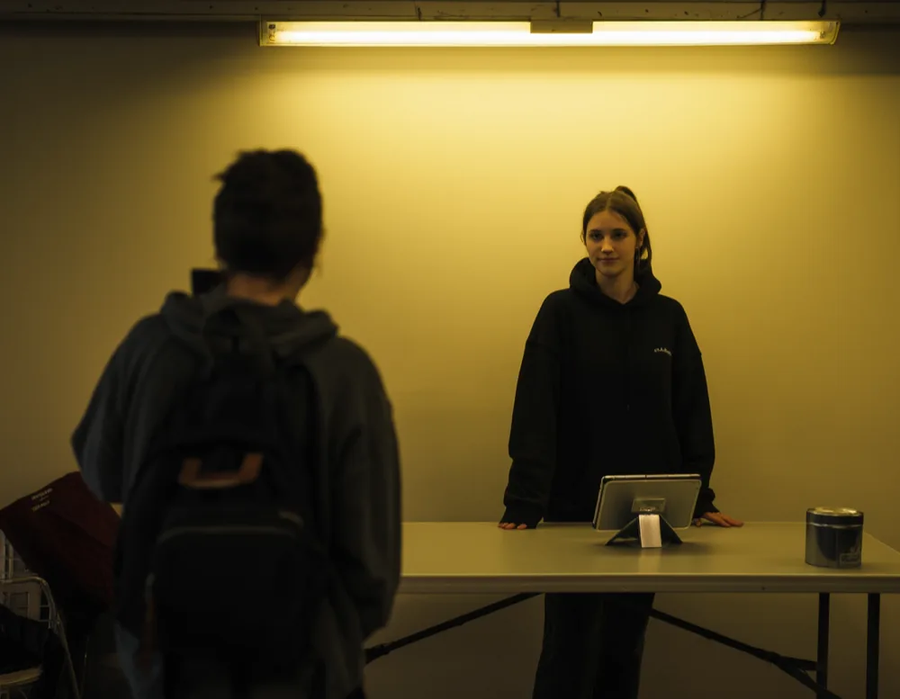 The desk by the door: a folding table, the check-in tablet and the cash tin, with two dancers waiting to pay